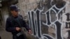 FILE - A member of the Salvadoran National Police walks next to symbol of the "Mara Salvatrucha" gang painted on a wall during an anti-gang operative in San Salvador, El Salvador.