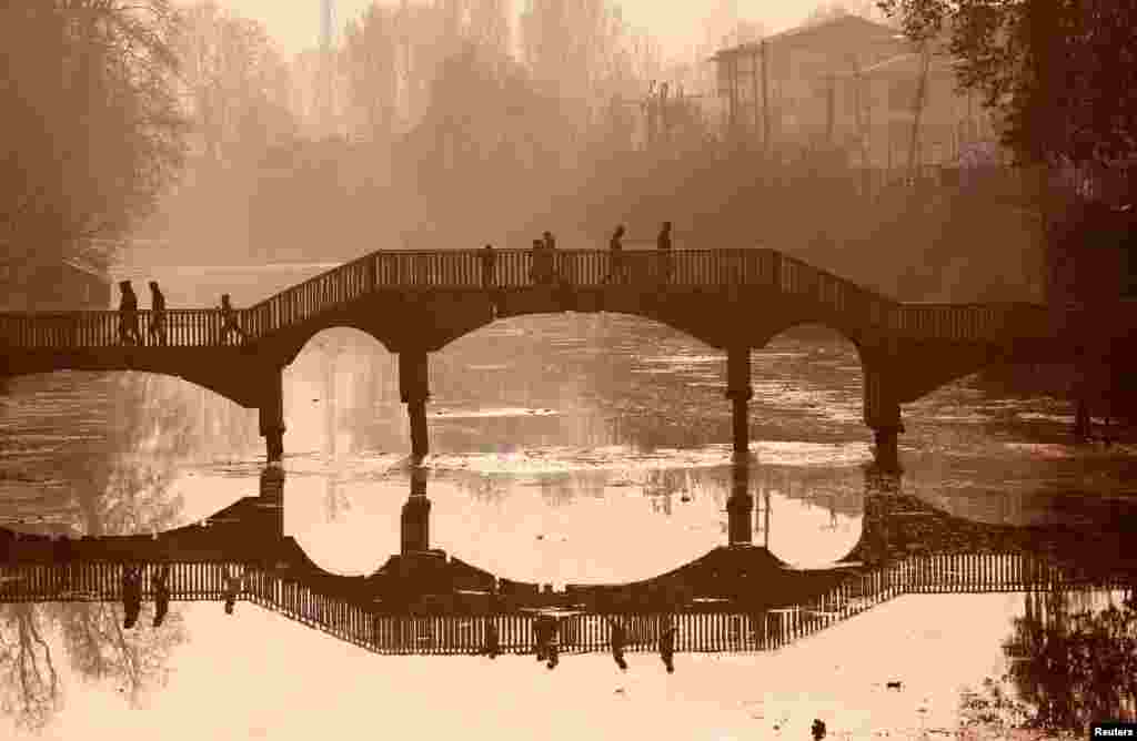 People walk on a wooden footbridge across a canal during an autumn day in Srinagar, India.
