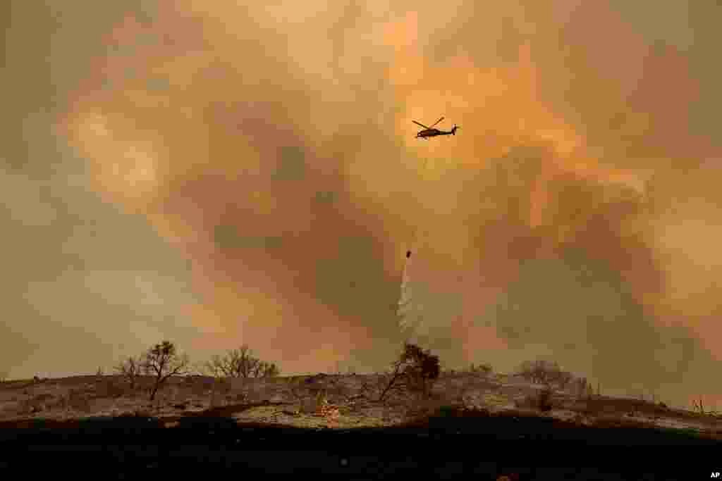 A helicopter drops water while trying to keep a wildfire from jumping Santa Ana Road near Ventura, California, Dec. 9, 2017.