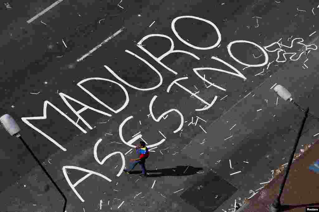 Um apoiante da oposição passa por cima de palavras escritas no asfalto de uma rua bloqueada, &quot;Maduro Assassino&quot;, na Praça de Altamira, em Caracas, Fev. 21, 2014. 