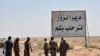 This photo released Sept 3, 2017 by the Syrian official news agency SANA, shows Syrian troops and pro-government gunmen standing next to a placard in Arabic which reads, "Deir el-Zour welcomes you," in the eastern city of Deir el-Zour, Syria. 